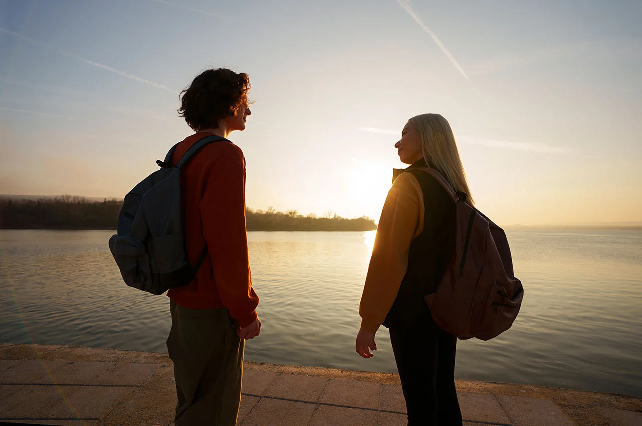 Two backpackers standing by lake at sunrise